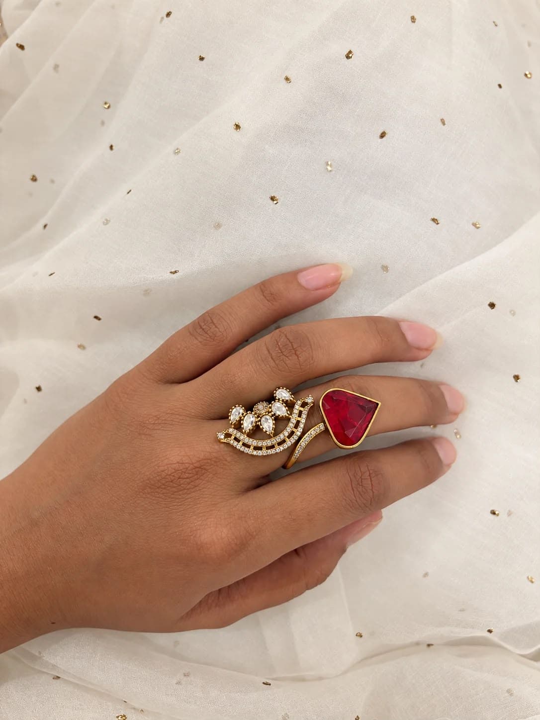 Bloom & Heart — An open ring: a spray of pear-cut stones at one end, a heart-cut red stone at the other, joined by a line of pavé.