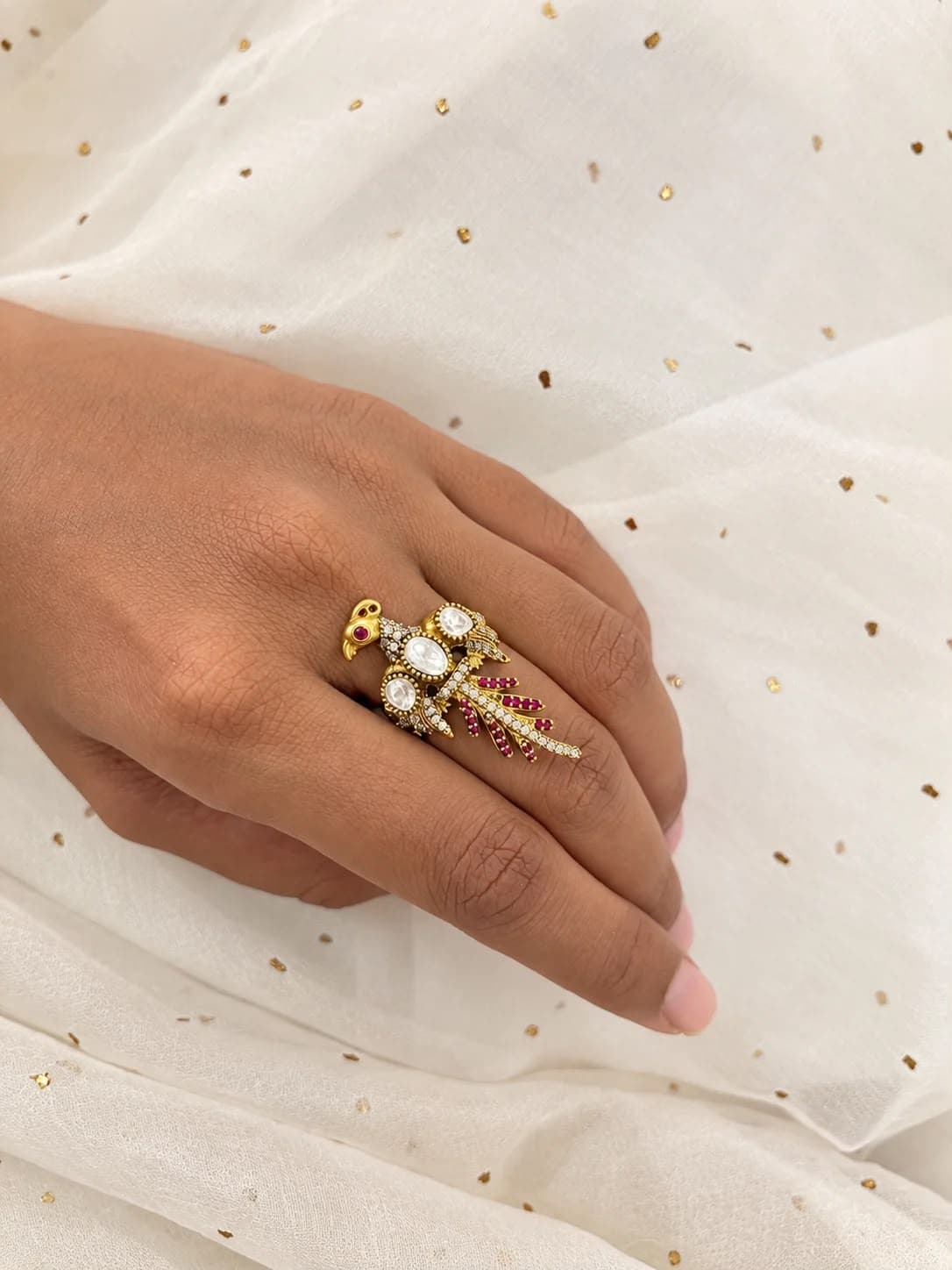 Tota — A parrot perched across the finger — polki on its breast, a red eye, and a tail of white and red stones fanning down the hand.
